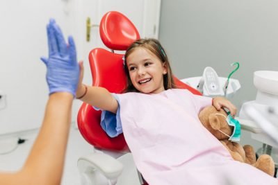 Cute little girl sitting on dental chair and having dental treat